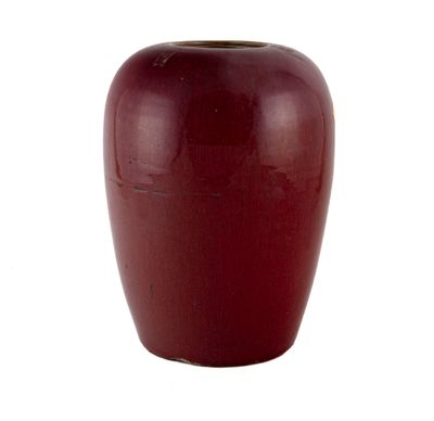 un vase rouge posé sur une surface blanche