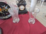 three glass vases sitting on a table with a clock in the background