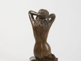 bronze statue of a woman sitting on a rock with her hands behind her head