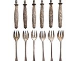 six forks and two spoons are arranged on a white surface