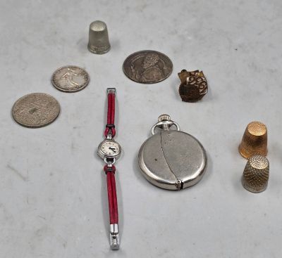 une montre en argent, un bracelet rouge, une montre en argent et une pièce en argent posés sur une surface blanche