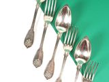 five silver spoons and two silver forks on a green and white background
