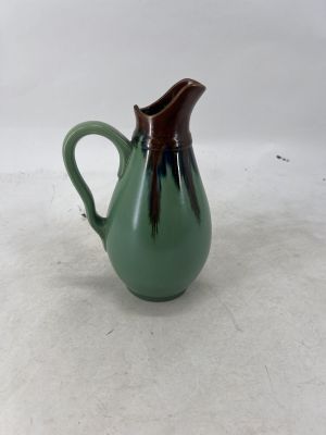 a green pitcher with a brown handle on a white surface