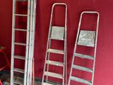 Plusieurs échelles sont alignées contre un mur rouge dans une pièce.
