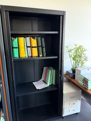 une bibliothèque noire sur laquelle sont posés de nombreux livres, dans une pièce