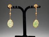 a pair of jade and gold earrings on a black stand