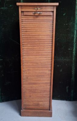 une grande armoire en bois surmontée d'un tiroir, devant un mur vert