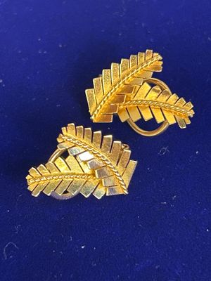 pair of gold tone leaf brooches on a blue background