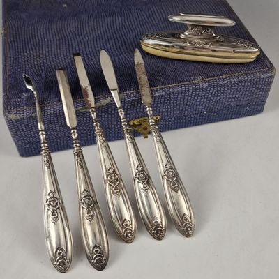 six cuillères et un couteau anciens en argent, posés sur une nappe bleue