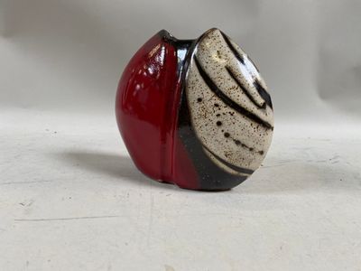 a red and black vase sitting on a white surface