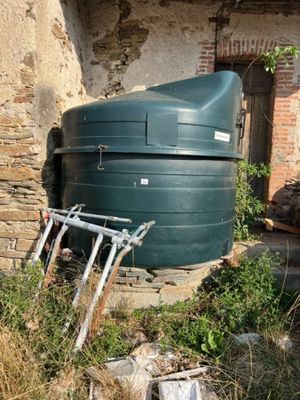un réservoir d'eau vert posé à même le sol, à côté d'un bâtiment en briques