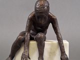 statue of a man sitting on a block with his hands on his knees