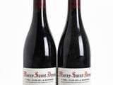 two bottles of red wine sitting next to each other on a white surface