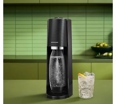 une machine à soda posée sur un plan de travail, à côté d'un verre de soda