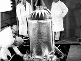 photo en noir et blanc de trois hommes en blouse de laboratoire travaillant sur un grand objet