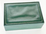boîte à bijoux en cuir vert posée sur une surface blanche, sur fond blanc
