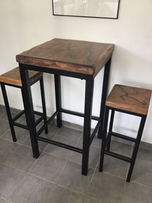 deux tabourets et une table dans une pièce où est accroché un tableau au mur