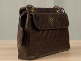 brown quilted leather handbag on wooden table with curtain in background