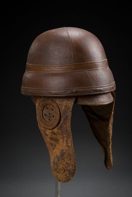 un casque en cuir marron posé sur un socle, sur fond noir