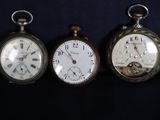 trois montres de poche anciennes sont alignées sur une surface noire