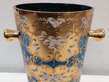 a gold and blue vase with handles on a white table