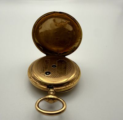 une montre de poche en or posée sur une surface blanche