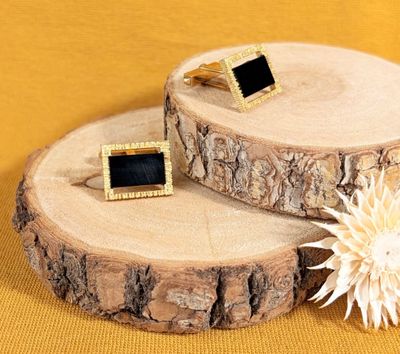 pair of black and gold cufflinks on a tree slice with a flower
