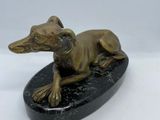 statue of a dog laying on a black base on a white surface