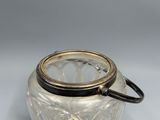 an antique glass jar with a lid and handle on a white surface