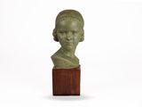 une photo représentant une sculpture verte représentant une tête de femme posée sur un socle en bois