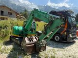 a green excavator that is parked next to a truck