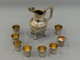 a silver pitcher and cups arranged in a circle