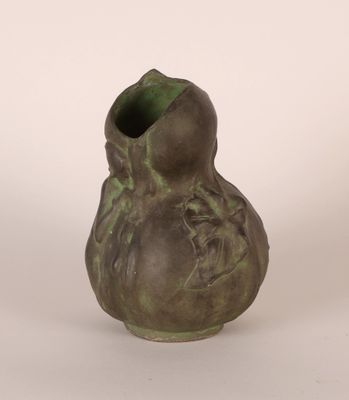 un vase vert orné d'un visage, posé sur un fond blanc