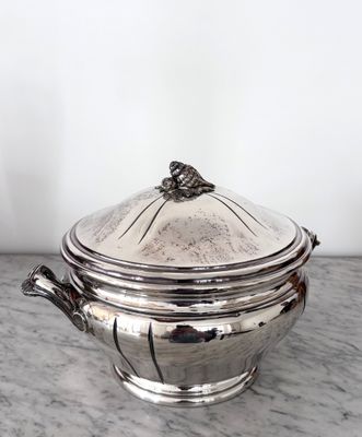 une cocotte ancienne en métal argenté avec son couvercle, posée sur une table en marbre