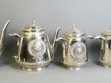 five silver teapots and a coffee pot are lined up on a table