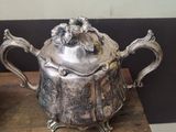 a silver teapot sitting on top of a table next to a plate