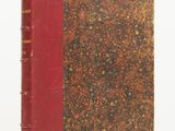 an old book with a red cover sitting on a white surface