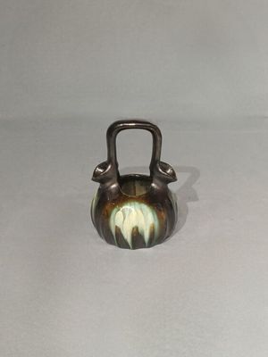 une image représentant une petite bouilloire en métal posée sur une surface blanche