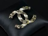 a close up of a black pillow with a silver chanel brooch