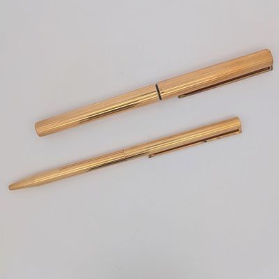 deux stylos dorés et un stylo à bille posés sur une surface blanche