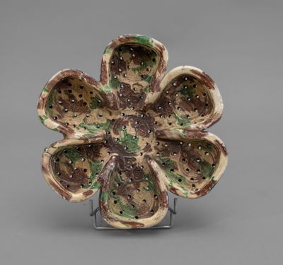 a small ceramic flower on a stand on a gray surface