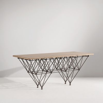 La table est en fil de fer et en bois, avec un plateau en bois.