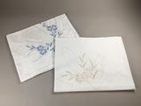 two white napkins with blue flowers on them sitting next to each other