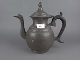 an antique silver teapot with a bird handle on a grey background