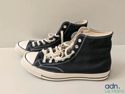 Des baskets Converse noires avec des lacets blancs sont posées sur une surface blanche