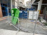 a green chair behind a metal fence on the sidewalk