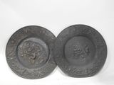 two black plates with designs on them sitting on a white surface