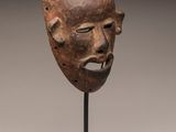 a brown mask on a black stand with a white background