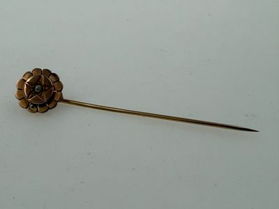 a gold pin with a flower on it on a white surface
