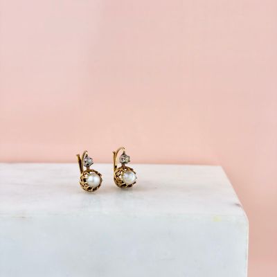 une paire de boucles d'oreilles en or ornées de pierres blanches, posées sur un bloc de marbre